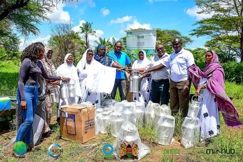 Women camel milk producers and project staff holding stainless-steel milk cans at an equipment handover