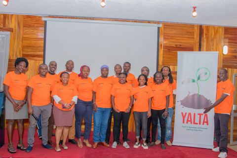 A group of young people in orange YALTA T-shirts standing beside a YALTA banner